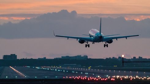 Airplane landing on illuminated runway during sunset