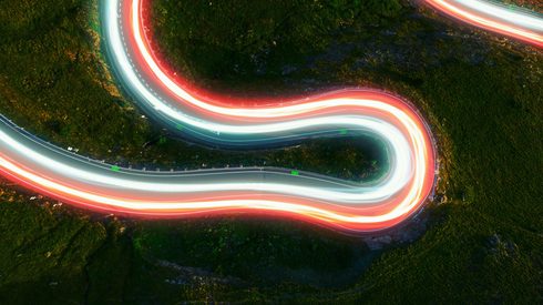 Electric light trails connecting destinations on a mountain road from a bird's eye view